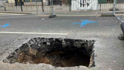 A hole appeared in Bury New Road. It is square-shaped and surrounded by fencing. 