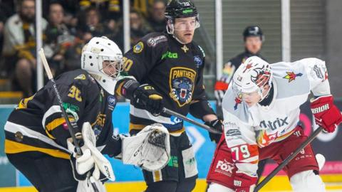 Cardiff Devils Ryan Barrow in front of Nottingham Panthers netminder Jason Grande and defenceman Zsombor Garat