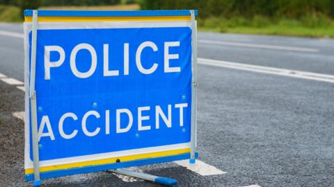 A generic stock image of a 'police accident' sign on a blue background on a tarmac road.