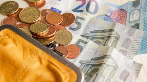 A yellow purse with Euro notes and coins spilling out.