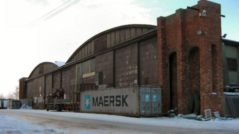Exterior image of hangars located the Aerodome in Hucknall, with a large shipping container placed next to the brick wall