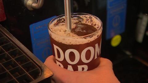 A pint of Doom Bar is being pulled by a barman in a pub. Doom Bar is an amber ale with a frothy top.