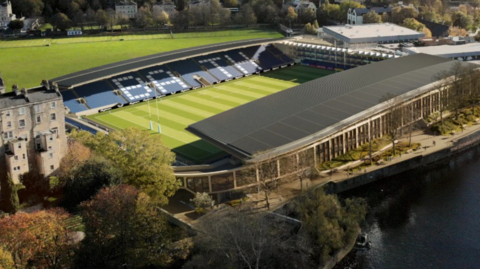 A generated image of a stadium with two large roofs covering the blue seats on the longer sides. White seats spell out BATH on one far side. The pitch is striped with green grass and has two rugby goals. A shaded river is seen in the foreground and behind is a green field.