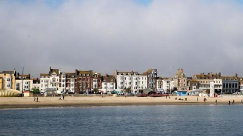 People walk on the beach as sea mist rolls in from the sea at Weymouth as the resort prepares for the start of the holiday season in Dorset, England.