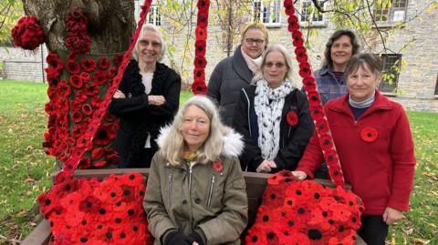 Shapwick Starlets Women's Institute members stood next to a church bench which is covered in knitted poppies.