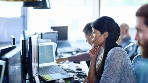 Woman sits at a desk filled with computers