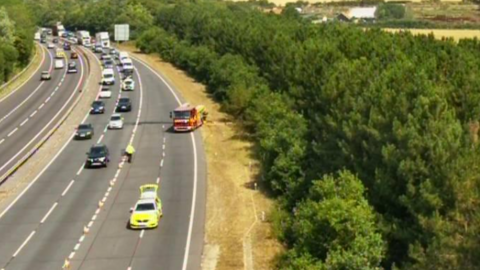 A traffic camera image of the A14 and a neighbouring woodland. On the eastbound carriageway is a fire engine and a police car. Cars have been stopped. 