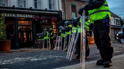 A line of riot police resting on their shields, on a Sunderland street, in front of the Vesta Tilleys public house