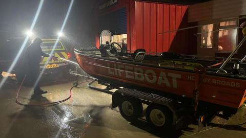 Hemsby inshore lifeboat being hosed down by a man during the middle of the night, following the rescue. It is outside a red lifeboat station.
