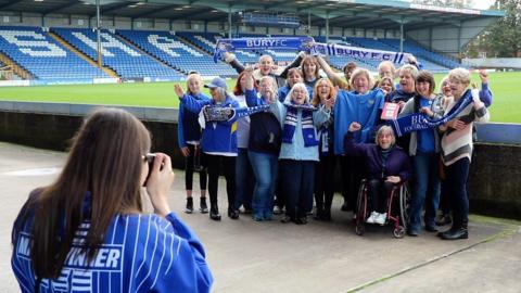 Female Bury FC having their photo taken inside the stadium at Gigg Lane.