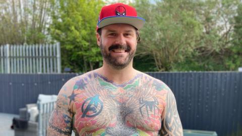 Man with tattoos over torso wearing a red hat
