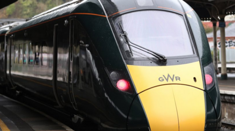 The front of a Great Western Railway train. It is dark green with a section of yellow below the front window.