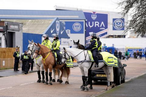 Four police officers on horses are in front of Fratton Park stadium in Portsmouth, other officers stand behind them closer to the ground