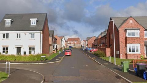 A narrow street with new homes on either side, one of them with a white front