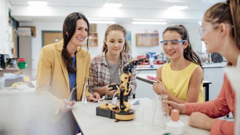 Female students and teacher in a classroom with a robotic device on the desk