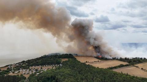 Large plumes of smoke rise from a coastal area in the distance