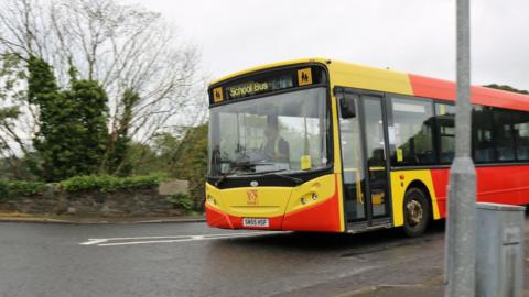 A school bus in Dumfries and Galloway with bright yellow and red livery on a road through a rural area