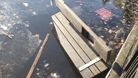 The remains of a broken wooden bench floating on the surface of a body of water surrounded by pieces of broken ice.