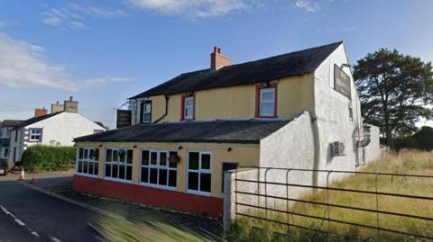 Google Maps image showing the Bird in Hand. It has windows running along the front of the building on the ground level and above. It is painted yellow and has a slate roof.