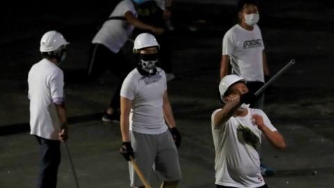 Men in white T-shirts with poles are seen in Yuen Long after attacked anti-extradition bill demonstrators at a train station, in Hong Kong