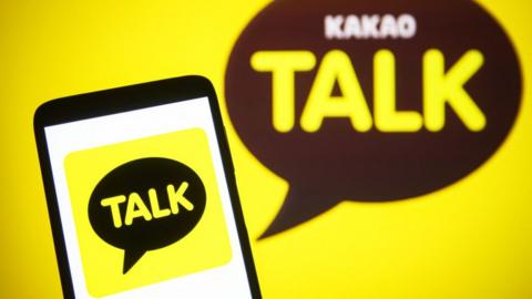 A KakaoTalk logo is seen on a smartphone and a pc screen.