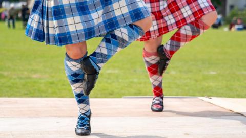 Legs of two Scottish dancers. One in blue kilt and sock, one in red.