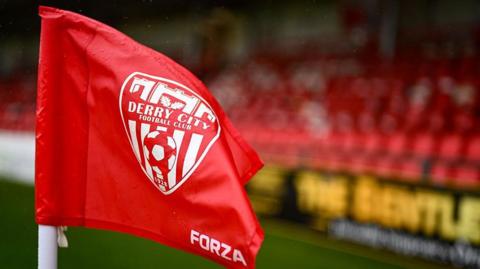 A red corner flag with the Derry City FC emblem is pictured inside the Brandywell