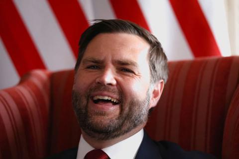 JD Vance sitting, laughing with a UD flag in the background