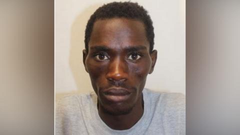 Marwan Jumaa has black curly hair and a grey prison sweatshirt and looks directly at the camera in what appears to be a police mugshot.