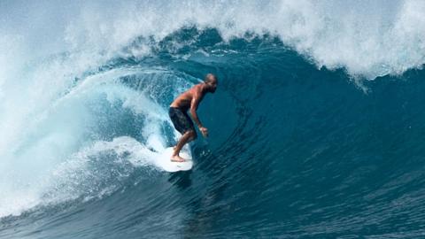 A surfer surfs though a tube formed by a large wave in the sea off the Mentawai islands