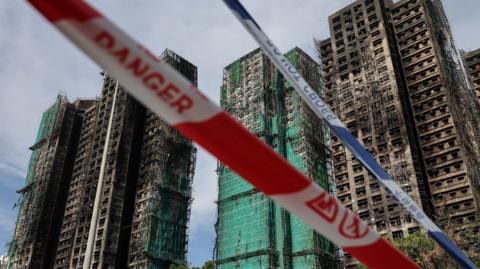 Damaged towers in the background. In front of it cutting through the image is red and white danger tape and blue and while police tape. It is day time