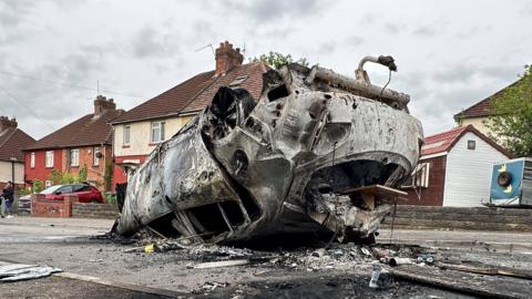 A burnt car flipped upside down in a residential street 