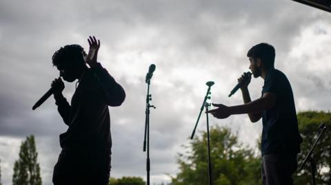 A shadow of two young men performing with microphones on a stage