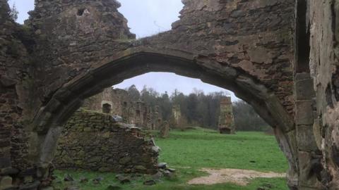 The view through a ruined archway on to a grassed area and more run down walls and parts of buildings