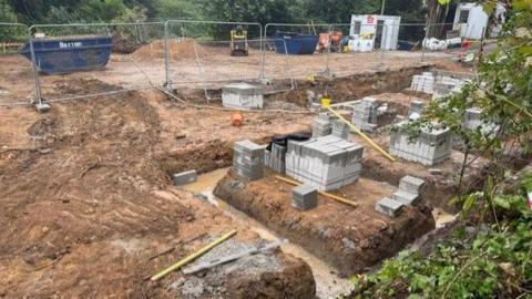 A building site. Large blocks have been placed on the soil. A metal fence blocks people from entering the site.