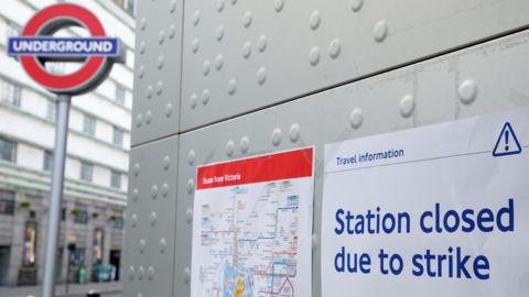A station closed sign attached to a wall in front of an Underground station, with another sign giving details of buses from Victoria next to it