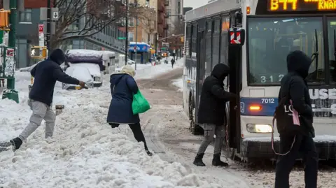 People jumping over mounds of snow to board a bus in New York.