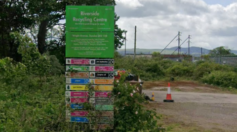 A green sign reading Riverside Recycling Centre with waste