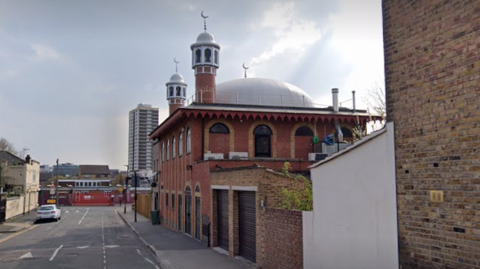 StreetView image showing the mosque on Brydges Road in Stratford. The mosque is a redbrick building with arched black windows with a dome and minarets on the roof