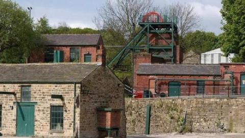 The National Coal Mining Museum building, with light and dark bricks as well as green doors, window frames and green ladders. 