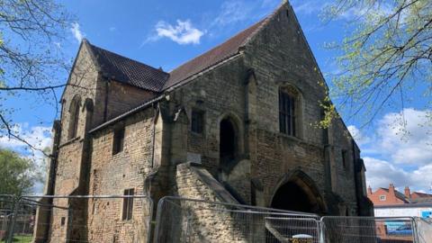 An old medieval brick gatehouse building surrounded by tall metal fencing.