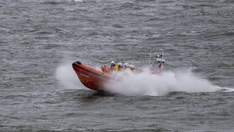 The Atlantic 85 Leicester Challenge III, an orange boat, on the water. White spray is around the boat. Four RNLI volunteers can be seen on the boat with yellow helmets and yellow jackets on.