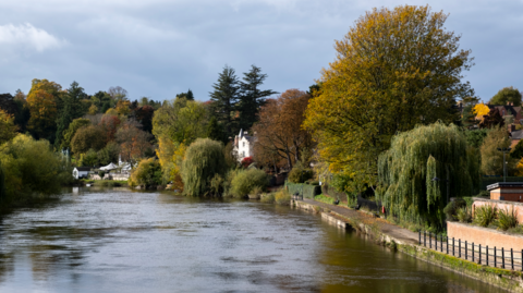 A wide river with trees along both sides and a footpath seen on the right hand side
