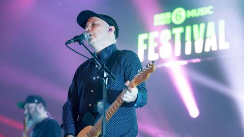 Mogwai performing on stage with pink lights and 6 music festival logo as backdrop