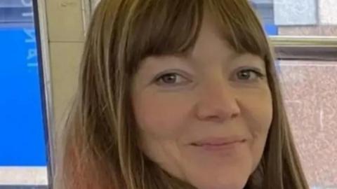 A woman with long light brown hair, smiles at the camera.