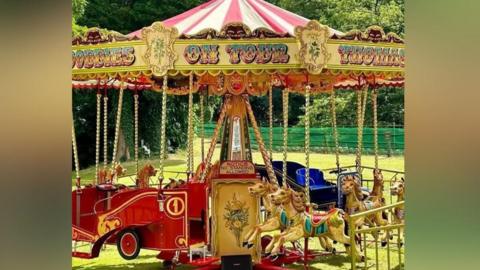 A vintage fairground roundabout ride with carousel horses and carriages. 