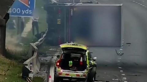 Lorry on its side on the M1 with police vehicle behind it