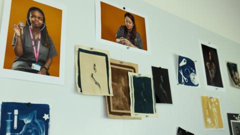Pictures part of the NHS Darkroom project pinned to a wall using pins. They include images of staff and images similar to radiographies or bodies and objects.