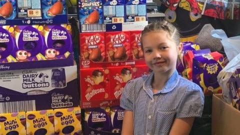 Ellie in her school uniform surrounded by stacks of Easter eggs in their boxes