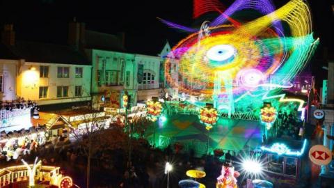 The town centre of Loughborough during the fair. There are stalls and a big spinning wheel. 